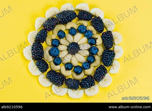 circular mandala arrangement of healthy berries fruits and nuts on a high contrast yellow background.