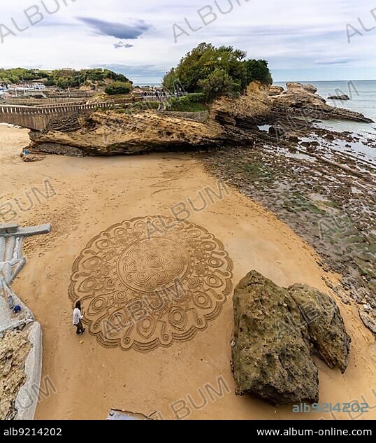 France - 21 October 2020: talented street artist draws mandala in the sand at the beach in Biarritz.