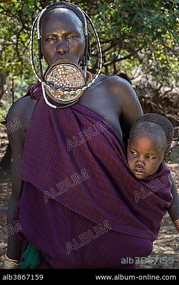 Woman with lip plate and headdress with baby, portrait, tribe of the Mursi, Southern Nations Nationalities and Peoples' Region, Ethiopia, Africa.