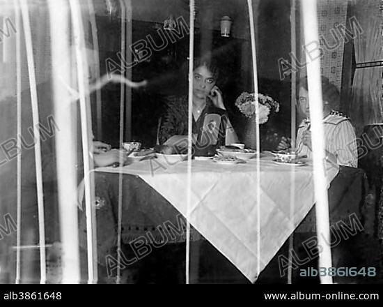 Family sitting at the dining table behind a curtain, photo of a family member in uniform on the table as a souvenir, World War I 1914-1918, Germany, Europe.