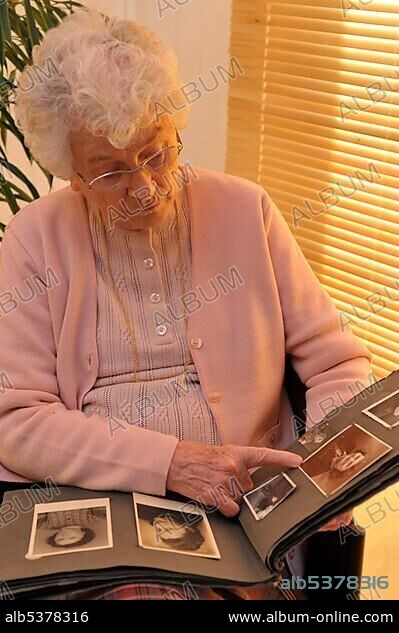 Elderly woman looking through photo album filled with old family portraits.