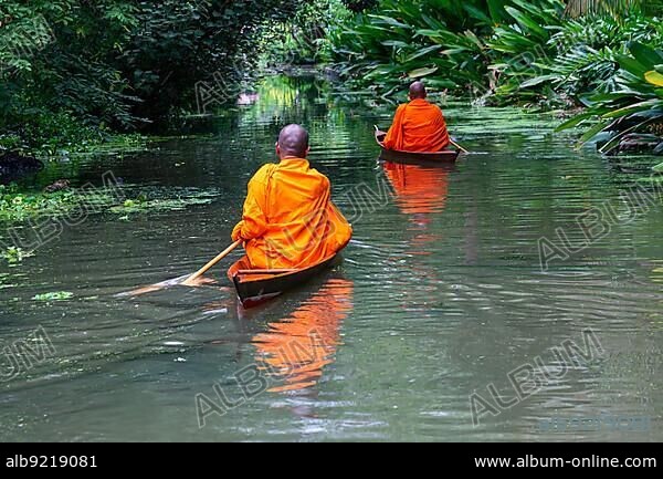 Buddhist monks paddle boat in the canal. Two monks row the small wooden boat in a canal to receive alms from Thai people in the morning.