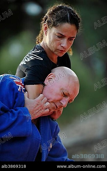 Woman is holding a man in a headlock during a martial arts training session in a park.