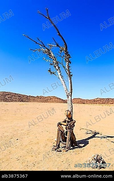 Cairn Lonely Man sits under a dried-up tree in Hartmann Valley, Kunene region, Namibia, Africa.