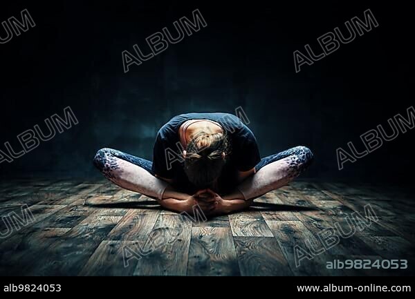 Young woman practicing yoga doing reclined goddess pose asana in dark room. Supta Baddha Konasana. Wellness and healthy lifestyle.