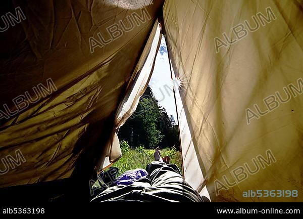 Legs peeping out of tent, hiker camping, column trail, perforated plate trail, hiking trail through forest, Green Belt, border trail, former German-German border, near Nordhalben, Bavaria, Germany, Europe.