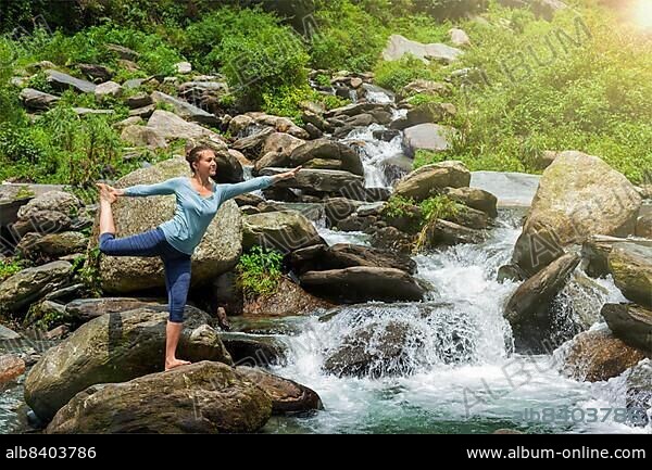 Yoga outdoors, woman doing yoga asana Natarajasana, Lord of the dance balance pose outdoors at waterfall in Himalayas.