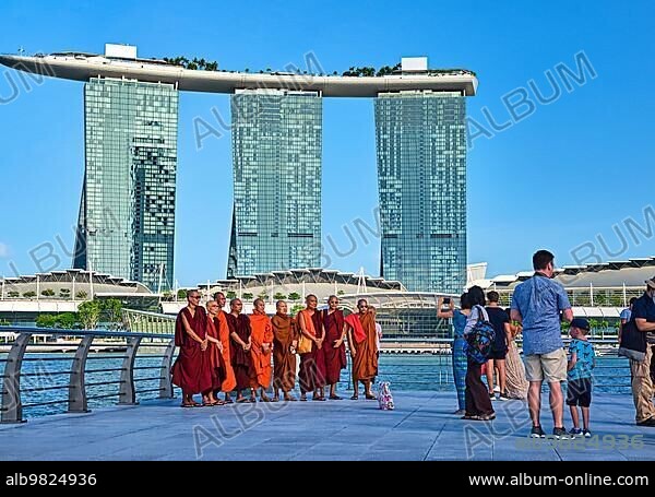 Singapore; Feb 25; 2020. Asian buddhist monks stand for group photo with iconic Marina Bay Sands and Shoppes mall in background. Tourists wait around for their turn. Bright sunny day; Asia.
