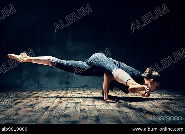 Young woman practicing yoga doing hurdler pose in dark room. Eka Pada Koundinyasana. Healthy; wellness and healthy lifestyle.