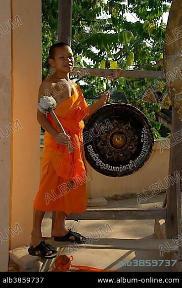 Buddhist novice monk wearing an orange robe hitting a gong, Wat Phonxay, Vientiane, Laos, Southeast Asia, Asia.