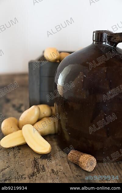 vintage moonshine jug on a rustic wooden table with potatoes and corn cob cork for distilling hard liquor.