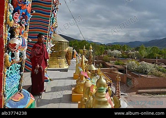 Tibetan Buddhist monk on a new painted and gilded chorten, stupa at the Wutun Si Monastery, Tongren, Repkong, Qinghai, formerly Amdo, Tibet, China, Asia.
