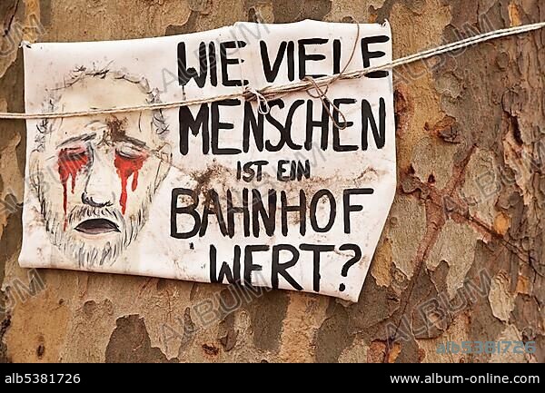 Protest poster "Wie viele Menschen ist ein Bahnhof wert?", German for "a train station is worth how many people?" on an old tree against the Stuttgart 21 railway project, Schlossgarten, castle gardens, Stuttgart, Baden-Wuerttemberg, Germany, Europe.