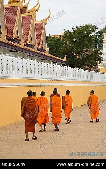 Buddhist monks dressed in orange robes walk along the wall of the Royal Palace, Phnom Penh, Cambodia, Asia.