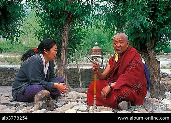 Buddhist monk holding a prayer mill, talking to a woman, Ladakh, Himalaya, North India, India, Asia.