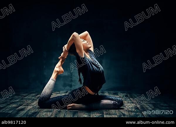 Young woman practicing yoga doing one legged king pigeon pose in dark room. Eka Pada Rajakapotasana asana. Wellness and healthy lifestyle.