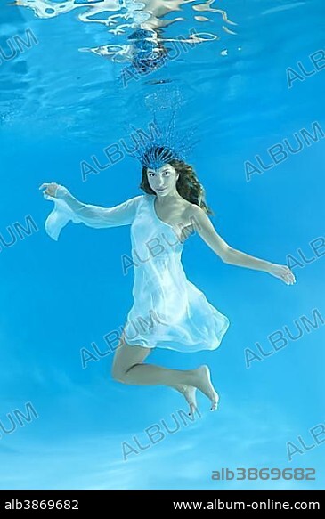 Ýoung woman in short, white dress wearing a crown poses under water, snow queen.
