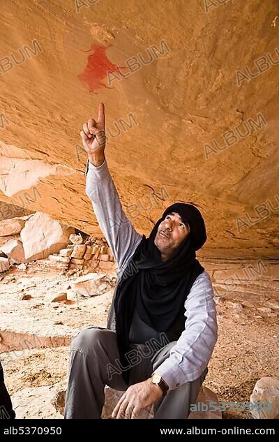 Tuareg pointing at prehistoric rock painting in the mountainous desert of the Akakus, Libya, Africa.