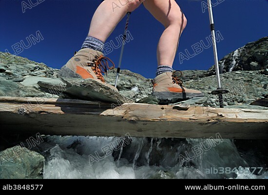 Hiker crossing a wooden bridge above a mountain brook, National Park Hohe Tauern, Tyrol, Austria, Europe.