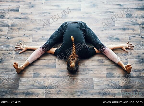Top view of young woman practicing yoga doing the turtle pose. Kurmasana asana. Wellness and healthy lifestyle.