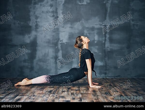 Young woman practicing yoga; doing cobra Pose Bhujangasana on dark background. sport and healthy lifestyle.