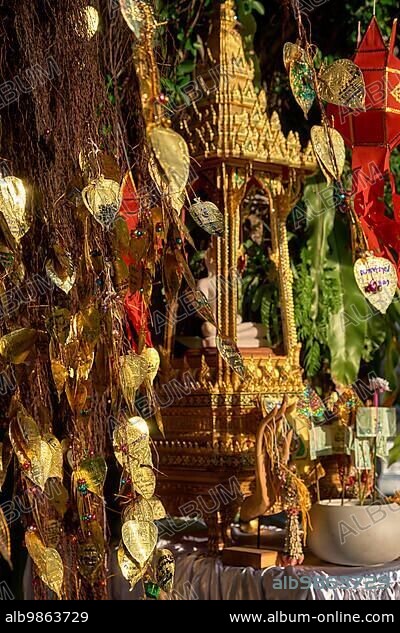 Traditional Thai Buddha altar as busabok with money and incense sticks offerings, colorful Lanna lanterns. Bodhi tree with golden leaves with wishes and promises in many languages. Selective focus, blurred background. Golden Mount, Bangkok, Thailand, Asia.