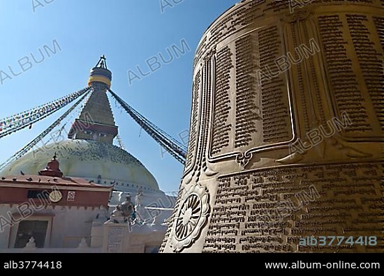 Big bell with Tibetan inscription, Boudnath Stupa at back, Kathmandu Valley, Kathmandu, Kathmandu District, Bagmati Zone, Nepal, Asia.