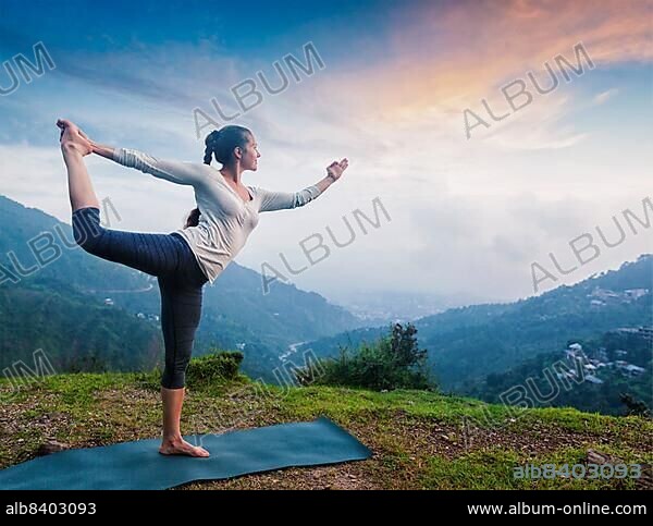Woman doing yoga asana Natarajasana, Lord of the dance pose outdoors at waterfall in Himalayas.