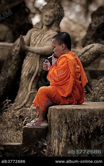 Monk smoking a cigarette in Buddha Park near Vientiane, Laos, Southeast Asia, Asia.