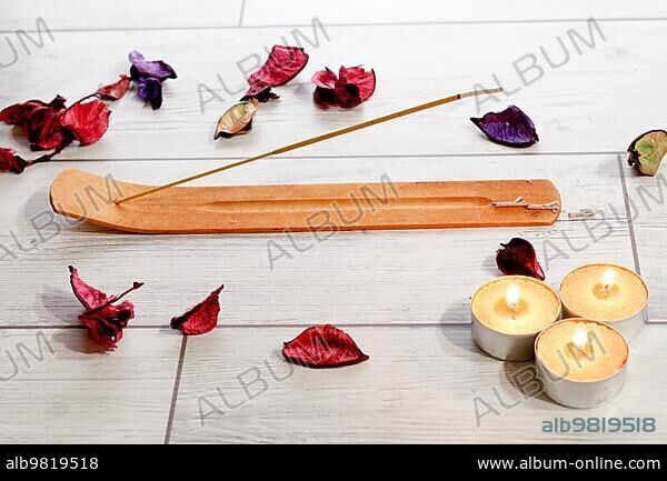 Close-up of an incense stick isolated on a white background with colorful flower petals and yellow candles.