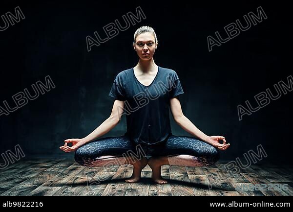Young beautiful woman doing yoga asana tiptoe pose prapadasana variation on dark room. Practicing yoga; wellbeing; wellness concept.