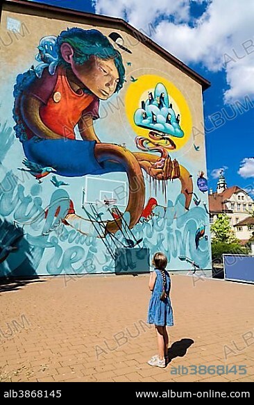 A colorful graffity with comic motive is painted at a house wall, a little girl is looking up to it, Würzburg, Bavaria, Germany, Europe.