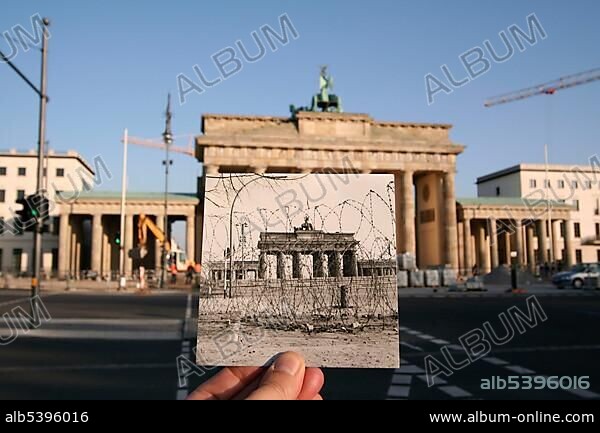 Then and now, hand holding an old black and white photo of Brandenburger Tor or Brandenburg Gate showing the Berlin Wall and barbed wire coils, Berlin, Germany, Europe.