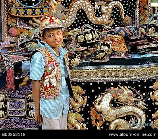 Boy with traditional textile art, tapestries and bags at a market, Tachilek, Shan State, Myanmar, Burma, Asia.