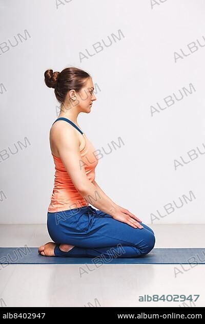 Woman in Hatha yoga asana Vajrasana, vajra pose or diamond pose on yoga mat on yoga mat in studio on grey bagckground.