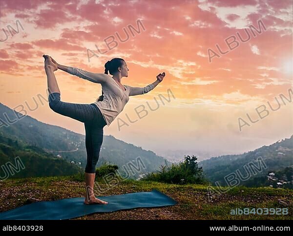 Woman doing yoga asana Natarajasana, Lord of the dance pose outdoors at waterfall in Himalayas.