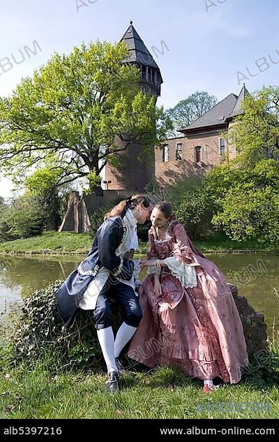 Young couple clothed in rococo style posing in front of the moated castle Linn, Krefeld, NRW, Germany, Europe.