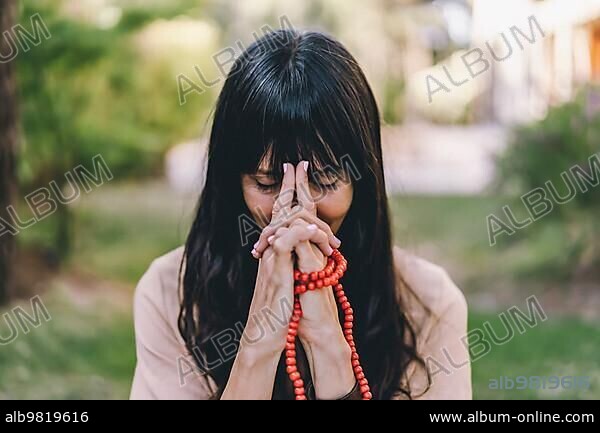 Woman practicing meditation sitting in yoga asana Kali Mudra holding a japa mala outdoors.
