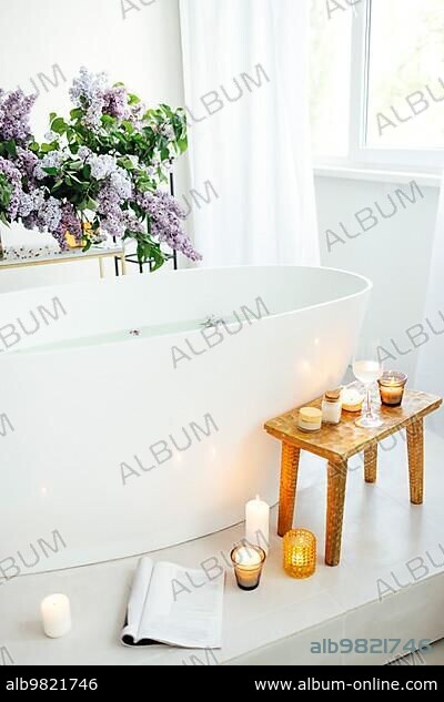 Modern bath room and spa center on the white tub wooden table. Candles and  magazine with vases with flowers. White background wall. - Album alb9821746