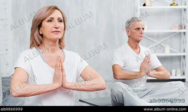 Healthy old couple sitting lotus pose with praying hands.