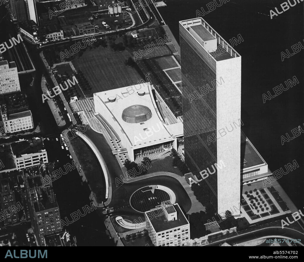 Aerial View Of United Nations Headquarters -- Black and white print of an aerial colour photograph of the Headquarters of the United Nations, in New York. This picture, taken from the South, shows all the U.N buildings (clockwise from top to bottom: the General Assembly, part of the Conference area along the river, the Secretariat and the Library) with, at left, the United Nations Plaza and, at right, the East River. January 1, 1954. (Photo by United Nations).