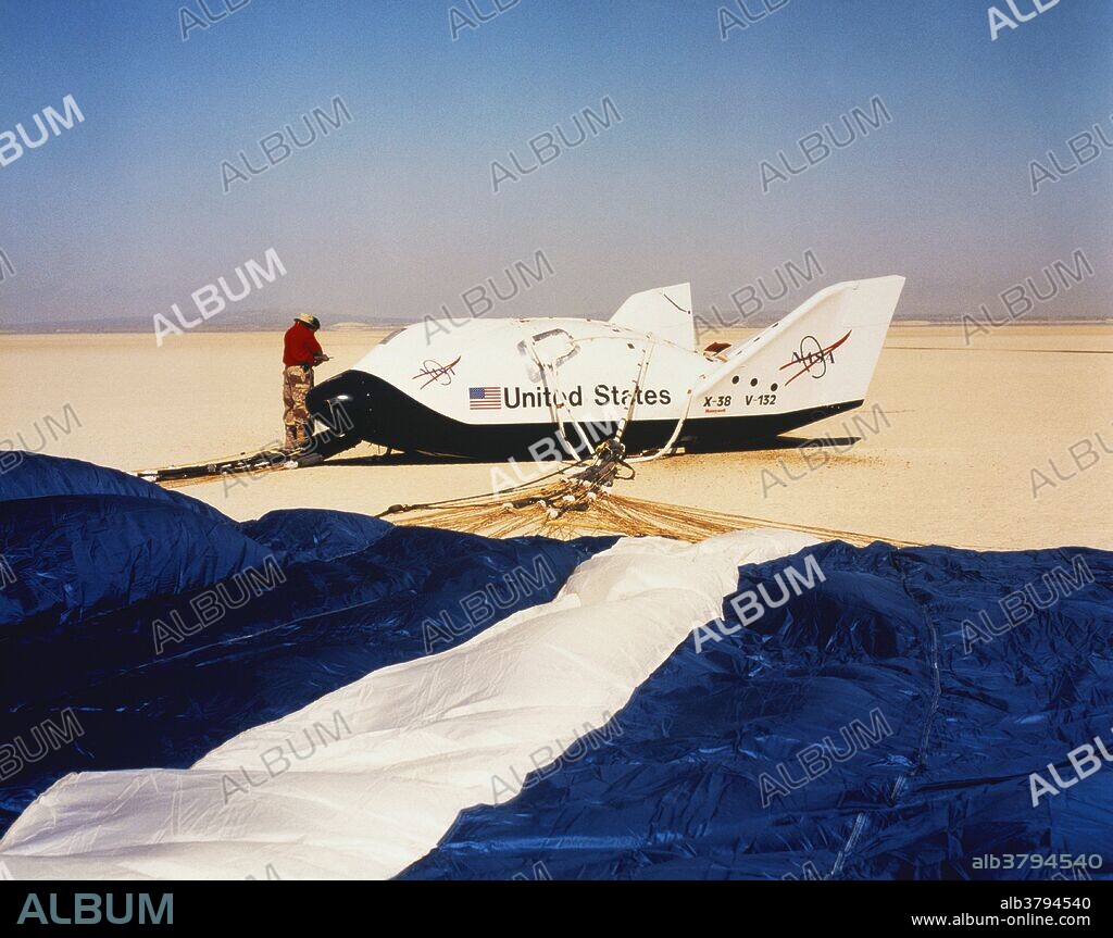 The NASA X-38 Crew Return Vehicle was a prototype for a wingless lifting body reentry vehicle that was to be used as a Crew Return Vehicle for the International Space Station (ISS). The X-38 was developed to the point of a drop test vehicle before its development was cancelled in 2002 due to budget cuts. Here, technicians examine the aircraft after landing on a dry lakebed. The parafoil parachute in the foreground steered the X-38 after it was released from a B-52 bomber; March 30th, 2000.