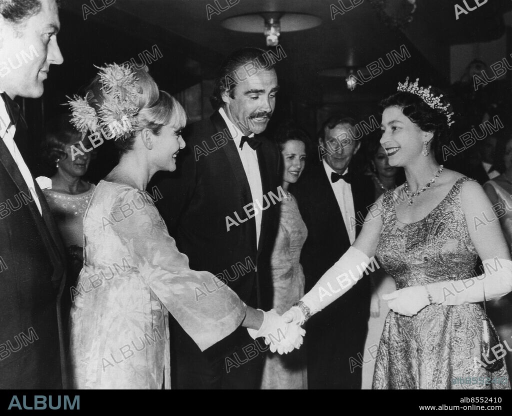 Orig. bildtext... MY LAST 007 ROLE- CONNERY TELLS THE QUEEN. James Bond, Secret Agent 007, met her majesty The Queen last night. The occasion was the premiere of the latest Bond thriller: You Only Live Twice, screened at the Odeon, Leicester Square, London. It was there that Bond, alias Sean Connery explained to the queen why he was resigning his 007 role. Did you feel you were where being typed? asked the queen. Yes, I'm afraid I did, grinned Sean. O.P.S H.M. The Queen shaking hands with Sean Connery's wife, Diane Cilento, after meeting 007 (on right). Anm. Diadem Handskar Klänningar Fjädrar Handslag Biopremiär persons: ELISABETH II, DROTTNING AV STORBRITANNIEN;DIANE CILENTO;SEAN CONNERY sites: LONDON;STORBRITANNIEN.