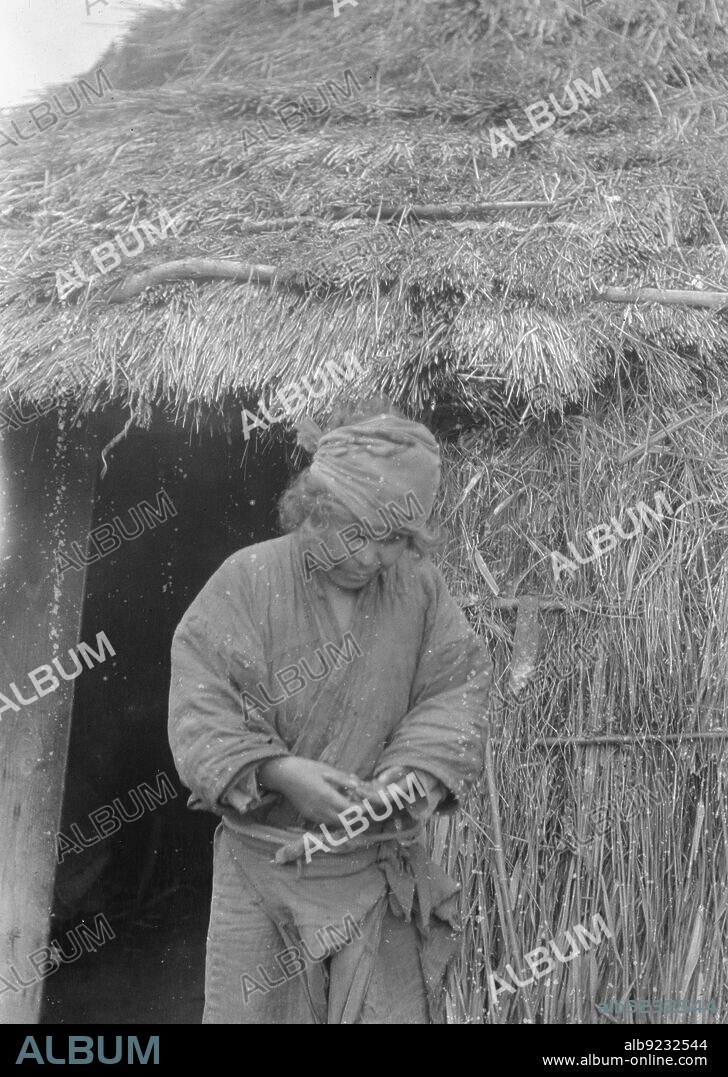ARNOLD GENTHE. Ainu woman standing outside the entrance of a hut, 1908.