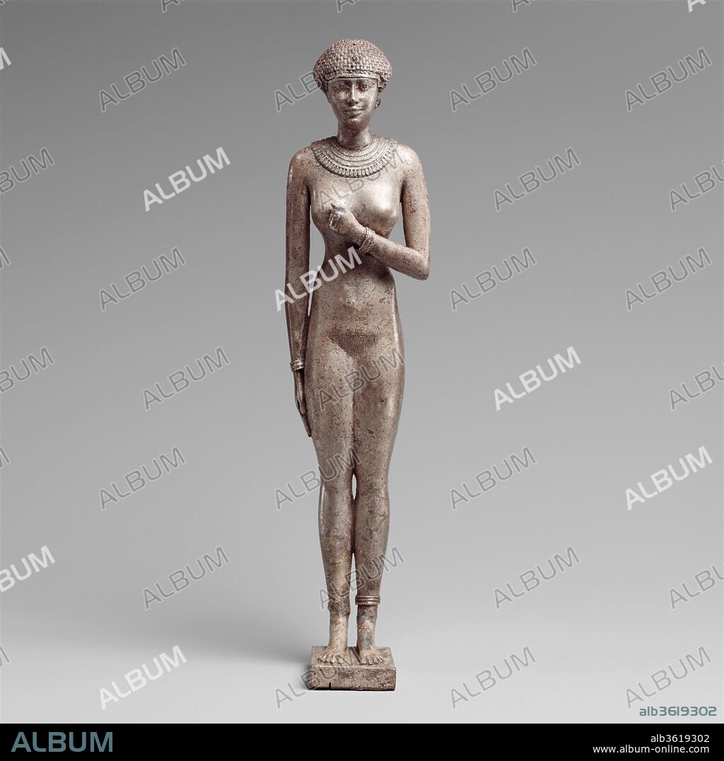 Statuette of a Royal (?)  Woman with the Cartouches of Necho II on her Arms. Dimensions: H. 23.8 cm (9 3/8 in.); W. 5.6 cm (2 3/16 in.); D. 5.4 cm (2 1/8 in.). Dynasty: Dynasty 26. Reign: reign of Necho II. Date: 610-595 B.C..
This nude sensual female figure has the cartouches of Necho II on her upper arms. A small tightly fitted wig caps her head, and two holes with silver wires are located in the wig over her forehead; their placement suits a uraeus. She wears a finely wrought broad collar plus earrings (only one of which is preserved), bracelets and anklets. 
King's cartouches are normally a sign affiliation for male courtiers; it is strange to see them on a nude female figure, and that she apparently also wore the uraeus. While nude female figurines have been for some time understood as requests for birth and rebirth based on texts on a few, new evidence has expanded our understanding, relating examples found in temples to the efficacy of rituals and magical cures and pointing to their identification with numerous goddesses. This magnificent figure might best be understood in relation to the important role of the God's Wife of Amun at Thebes. In the Saite period she was the daughter of a king established as the god's consort and responsible for stimulating his generative powers for the good of all.
Purchased in Thebes, it is possible the figure derives from Karnak or from the burial of one of the God's Wives on the West Bank.