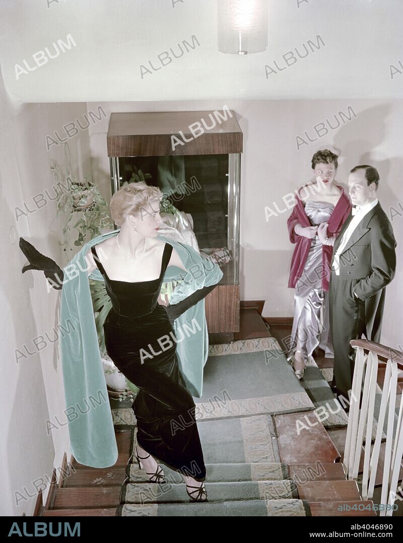 Female model shows an evening dress, Stockholm, 1950s. Watched by another female model and a male model in a tailcoat.