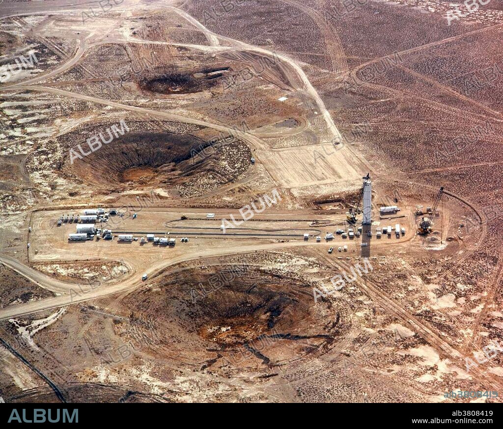 The Nevada National Security Site (NNSS), previously the Nevada Test Site (NTS), is a United States Department of Energy reservation located in southeastern Nye County, Nevada. Formerly known as the Nevada Proving Grounds, the site was established on January 11,1951 for the testing of nuclear devices, covering approximately 1,360 square miles of desert and mountainous terrain. During the 1950s, the mushroom clouds from the 100 atmospheric tests could be seen for almost 100 miles. The Nevada Test Site contains 28 areas, 1,100 buildings, 400 miles of paved roads, 300 miles of unpaved roads, ten heliports, and two airstrips. The vast majority of nuclear tests, 828 in all, were underground. Aerial view of preparations for an underground atomic bomb test. Craters caused by subsidence after previous underground nuclear explosions lie around the test site. The craters vary is depth and diameter, depending upon the weapon's size and burial depth, as well as the geology of the area immediately around it. Undated.