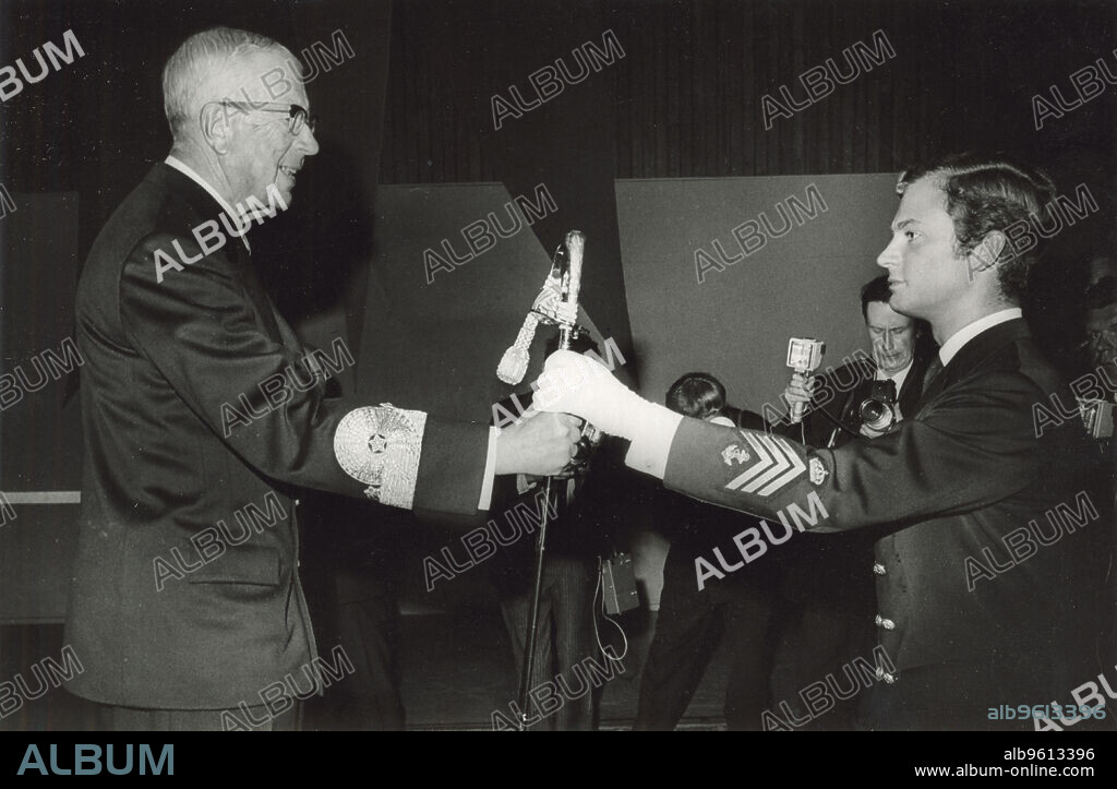 Crown Prince Carl Gustaf and his grandfather, King Gustaf VI Adolf of Sweden, 1968. The son of of Prince Gustaf Adolf, Duke of Västerbotten and Princess Sibylla of Saxe-Coburg and Gotha, Carl XVI Gustaf (1946-) became King of Sweden in 1973, succeeding his grandfather, who is seen here presenting him with a sabre as he is appointed an ensign in the military. From the collection of Svenskt Fotoreportages.