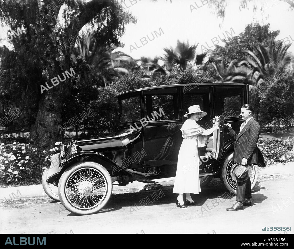 A 1916 Dodge 4, (1916?). A man holds a door open for a woman. In 1903 the Dodge brothers equipped their bicycle and car parts plant to build engines for Ford in return for a 10% interest in the Ford Motor Company. In 1914 they formed their own company, Dodge Brothers Inc. When asked why they wanted to build their own cars John Dodge replied, 'Just think of all the Ford owners who will someday want an automobile'.