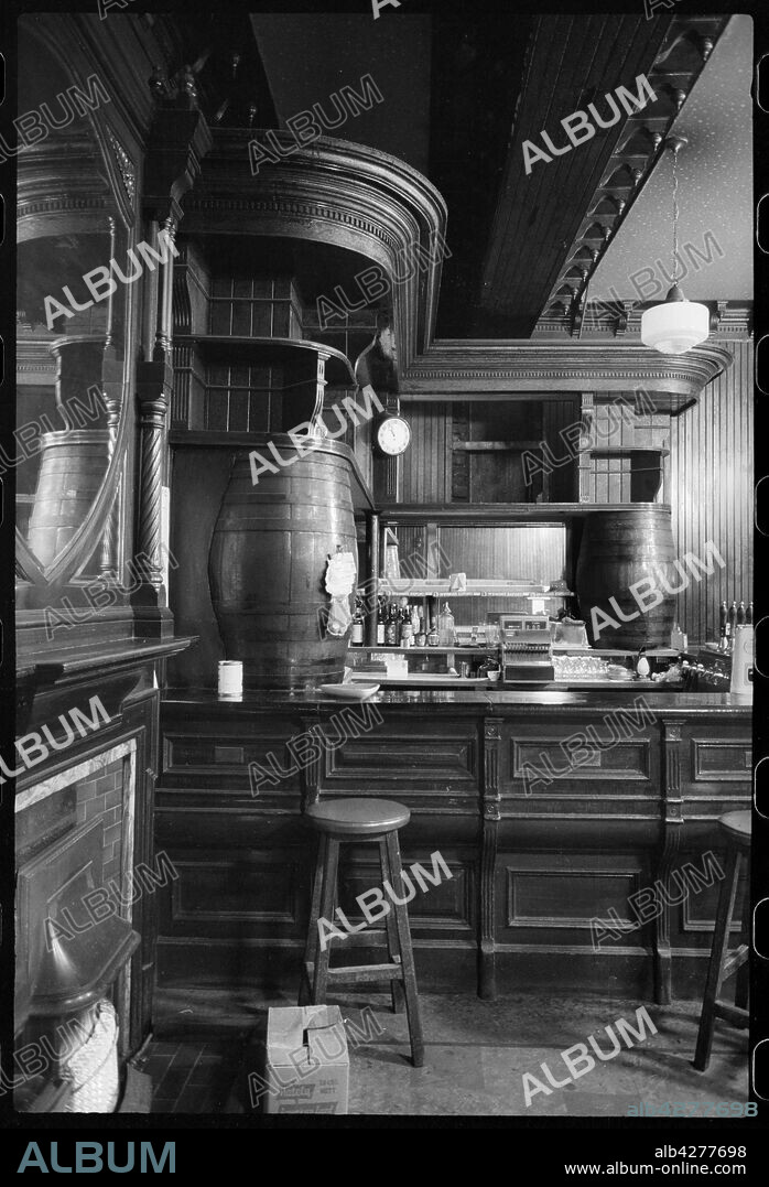 URSULA CLARK. Bar of the Royal Turk's Head Hotel, 73 Grey Street, Newcastle upon Tyne, c1955-c1980. The building that the Turks Head was situated had been built for Richard Grainger in c1837, and has been used as a location for houses, shops and a hotel. The image shows a curved bar in the corner of the room, with shelving built along the walls and supported at each end by barrels. There are bar stools on the customer side, and a mirror above a fireplace in the foreground.